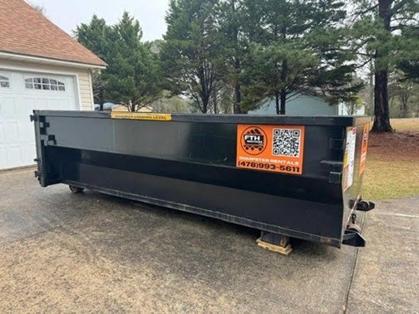 A black dumpster provided by FTH Services on a residential driveway.